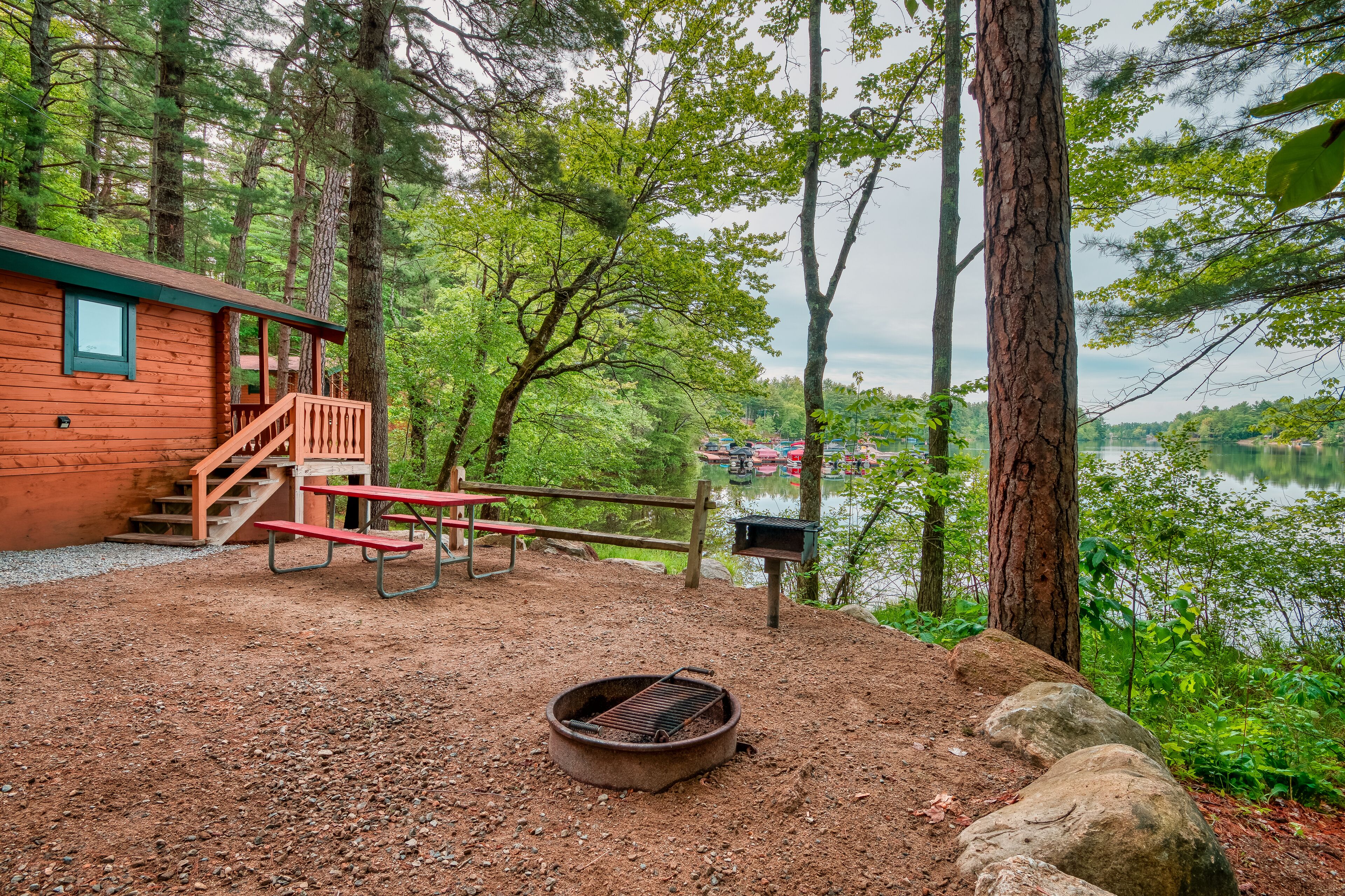 Een chalet met terras, picknicktafel en vuurplaats, omringd door bomen en een meer.