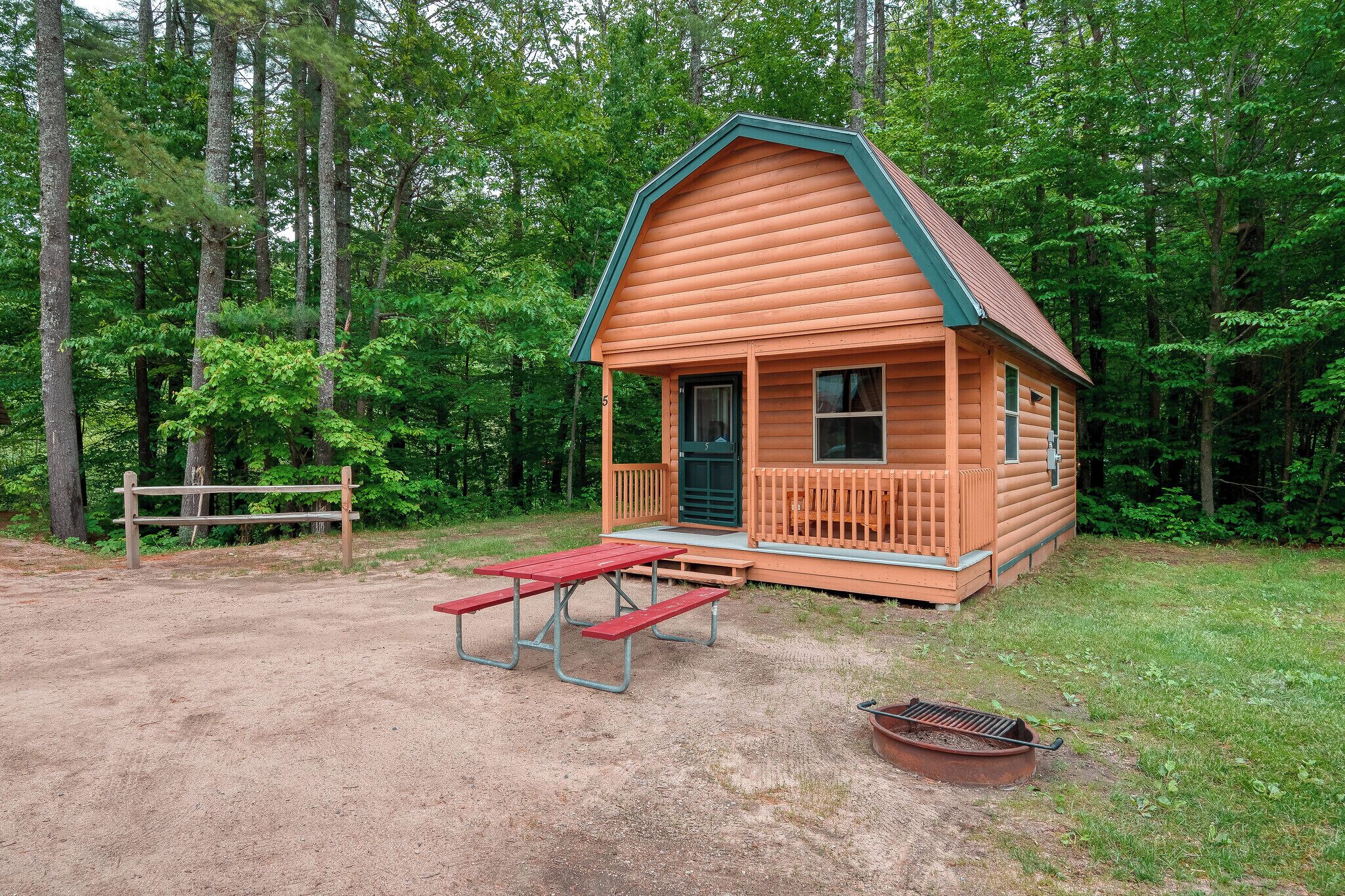 A small wooden cabin with a porch and picnic tables, surrounded by a forest.