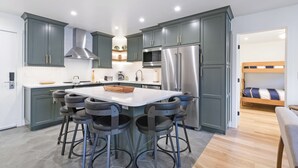 Een moderne keuken met grijze kastjes, roestvrijstalen apparatuur en een centraal eiland met barstoelen.