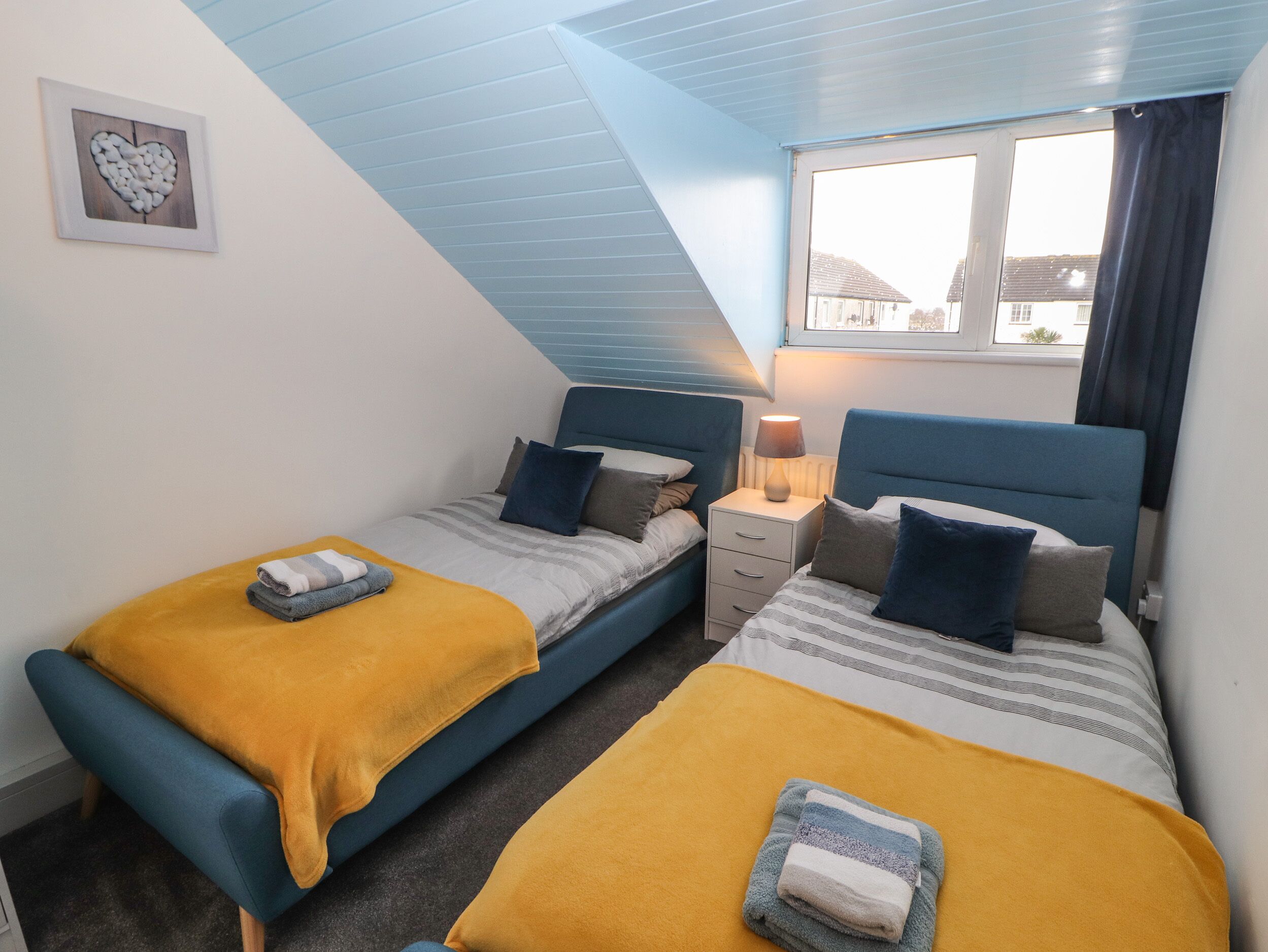 A bedroom with two beds, a window, and a bedside table with a lamp.
