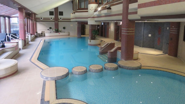 En indendørs swimmingpool med flere niveauer, siddepladser og flisegulv.