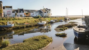 Et flodlandskab med både fortøjet langs bredden, en græsklædt skråning og en række huse med forskellige arkitektoniske stilarter.