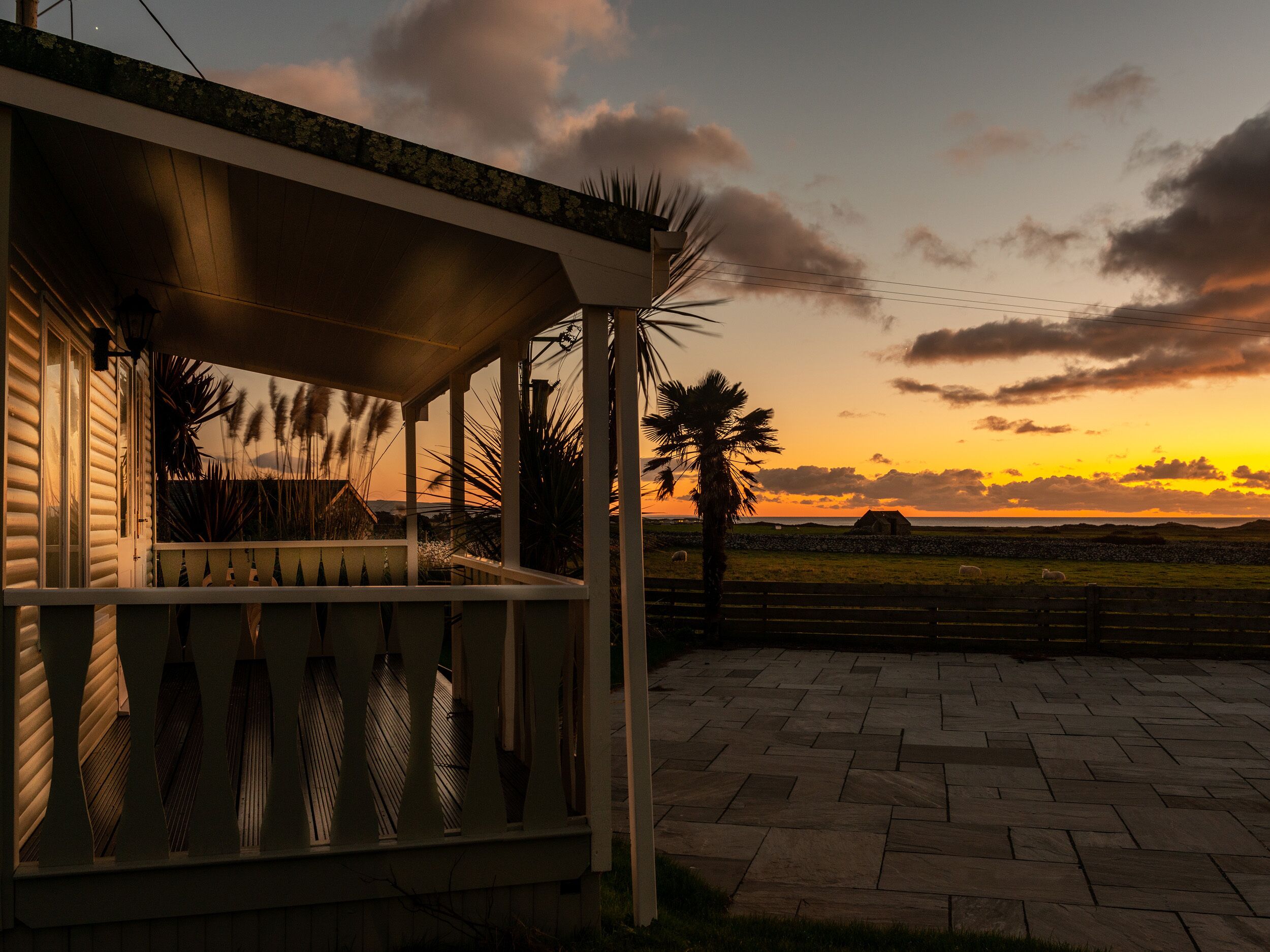 A covered outdoor area with a view of the sunset over a grassy field and a distant building.