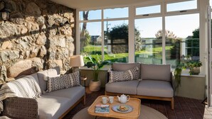 A cozy living room with a stone wall, large windows, and a comfortable seating area with a coffee table. - Bennar Fawr (Dyffryn Ardudwy)