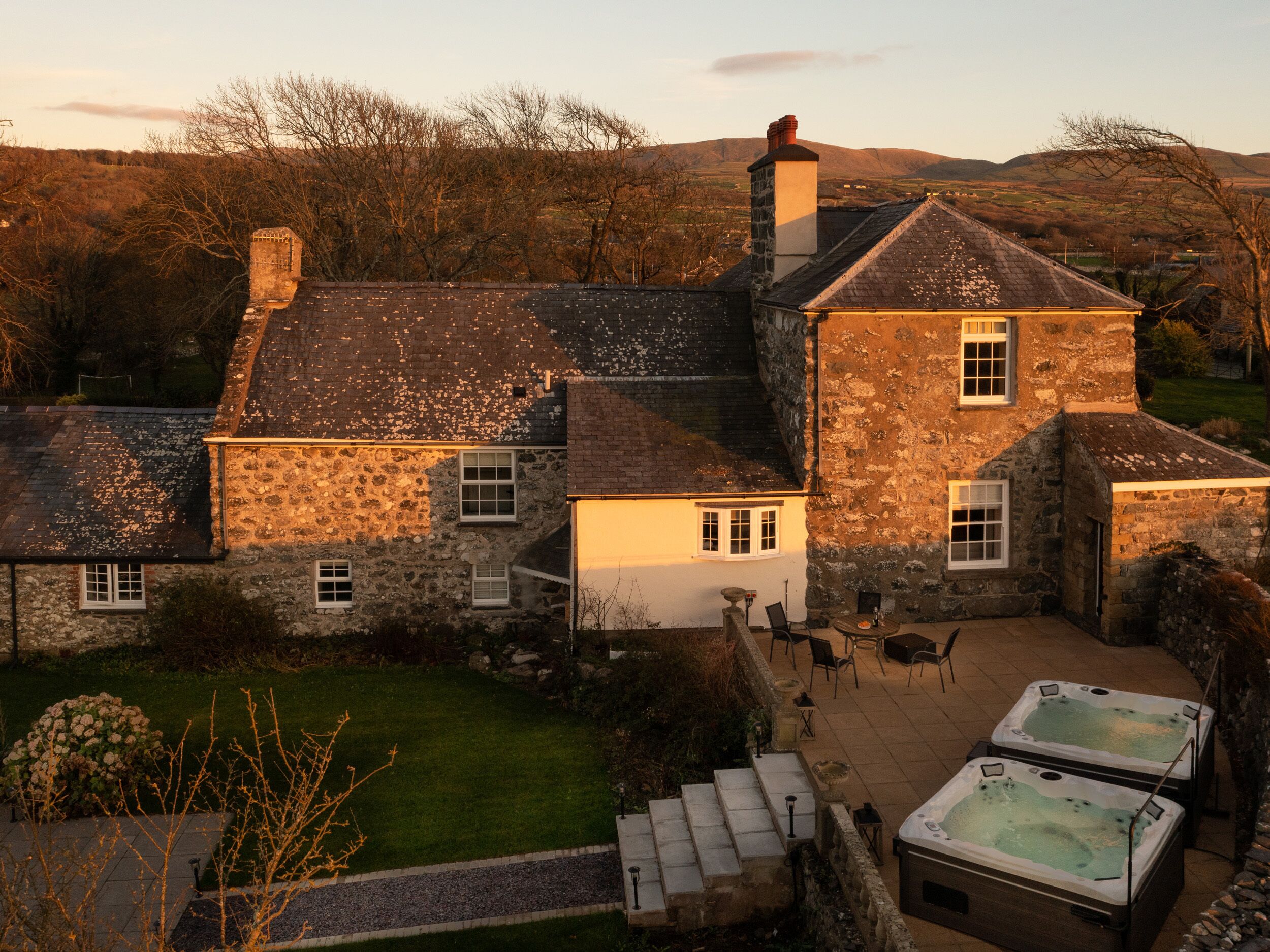 A stone house with a large patio area, including outdoor seating and two hot tubs.