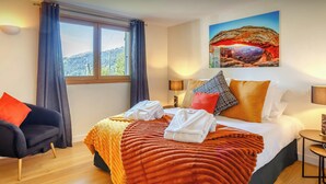 A hotel room with a bed, a chair, a window, and a painting on the wall. - Chalet Joux Verte - beautiful ski base for 8 with spa - OVO Network (Les Gets)