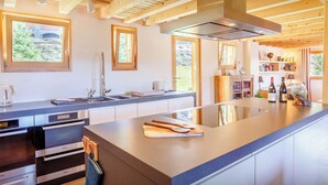 A modern kitchen with wooden beams, a large island, and a view of greenery outside. - Chalet Joux Verte - beautiful ski base for 8 with spa - OVO Network (Les Gets)