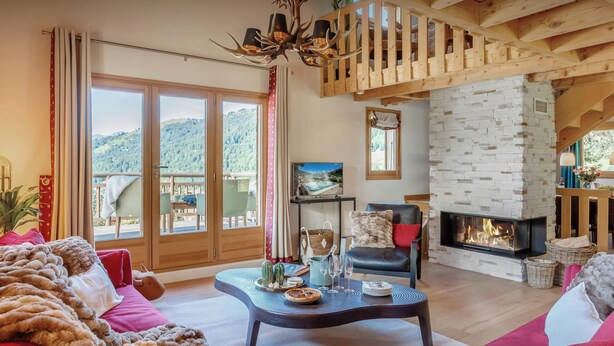 A cozy living room with a fireplace, a dining area with a table set for two, and a balcony with a scenic mountain view. - Chalet Joux Verte - beautiful ski base for 8 with spa - OVO Network (Les Gets)