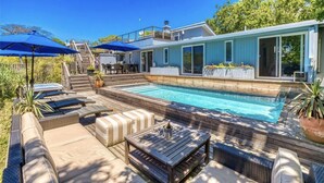 Ein modernes Haus mit Pool, Sitzgelegenheiten im Freien und einer überdachten Terrasse.