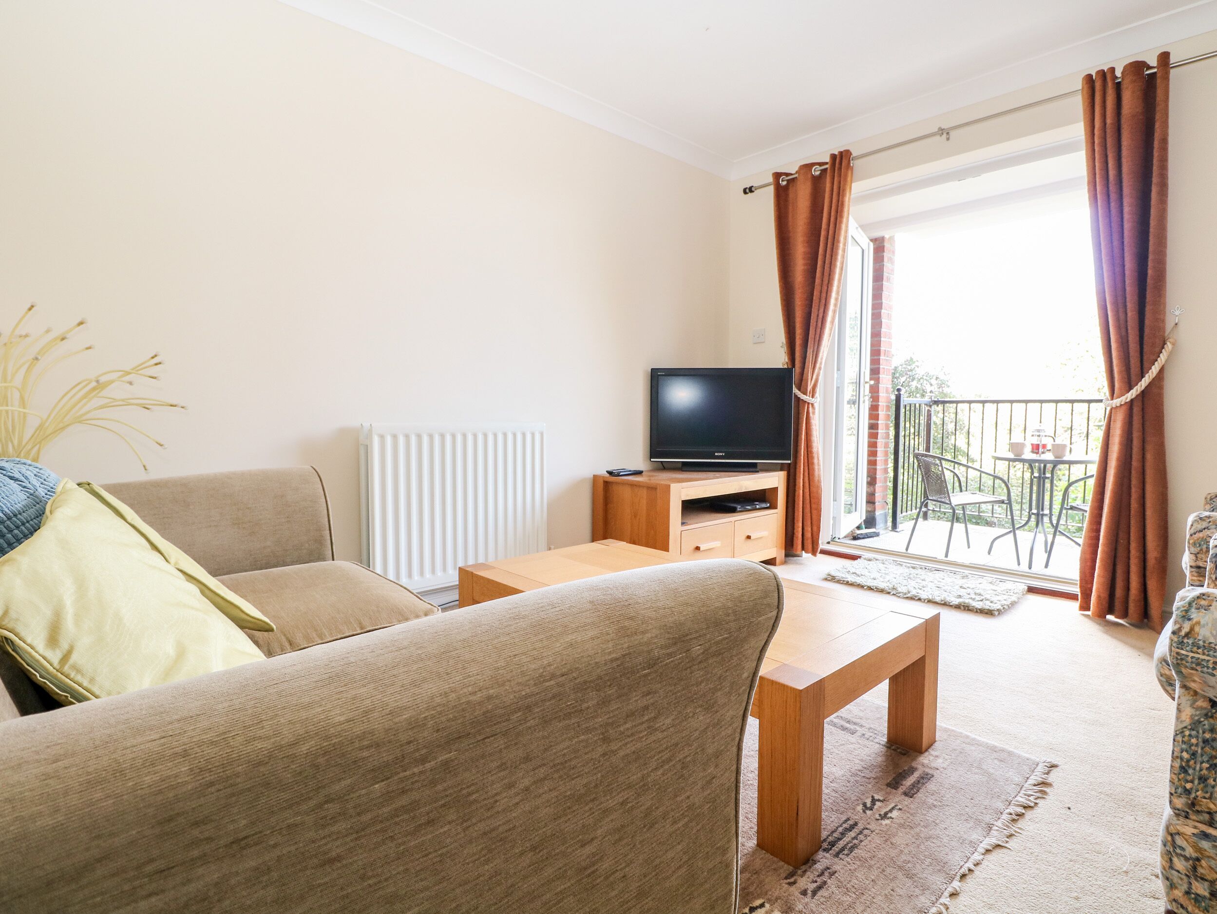 Ein Wohnzimmer mit Sofa, Couchtisch, Fernseher auf einem Holzgestell und einem Balkon mit Tisch und Stühlen.