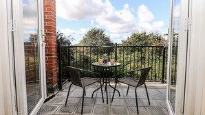 Een balkon met een tafel en stoelen, een glazen deur en uitzicht op bomen en lucht.