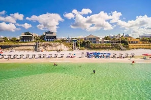 Ein Strandresort mit klarem türkisblauem Wasser, Strandsonnenschirmen und verschiedenen Gebäuden im Hintergrund.