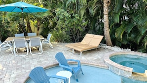 Un área de piscina con sillones de descanso, una mesa y sombrillas.