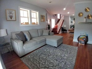 Un salon avec un canapé d’angle gris, un tapis à motifs et un escalier menant à un autre niveau.