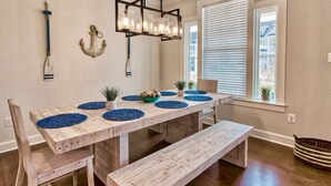 Een eetgedeelte met een houten tafel, blauwe placematen en een hanglamp.
