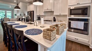 Een moderne keuken met witte kastjes, een centraal eiland met blauwe placemats, en roestvrijstalen apparatuur.