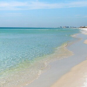 A beach with clear water, a sandy shore, and buildings in the distance. - 30A Gulf View Condo | Beach Access + 3 Pools (Santa Rosa Beach)
