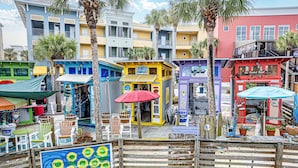 Un passeig marítim colorit amb diverses botigues i restaurants, seients de fusta i palmeres.