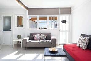 A modern living room with a grey sofa, a red sofa, a coffee table, and a window with blinds.