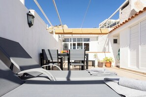 Une terrasse extérieure ensoleillée, avec des fauteuils, une table et des chaises, ainsi que des plantes en pot.