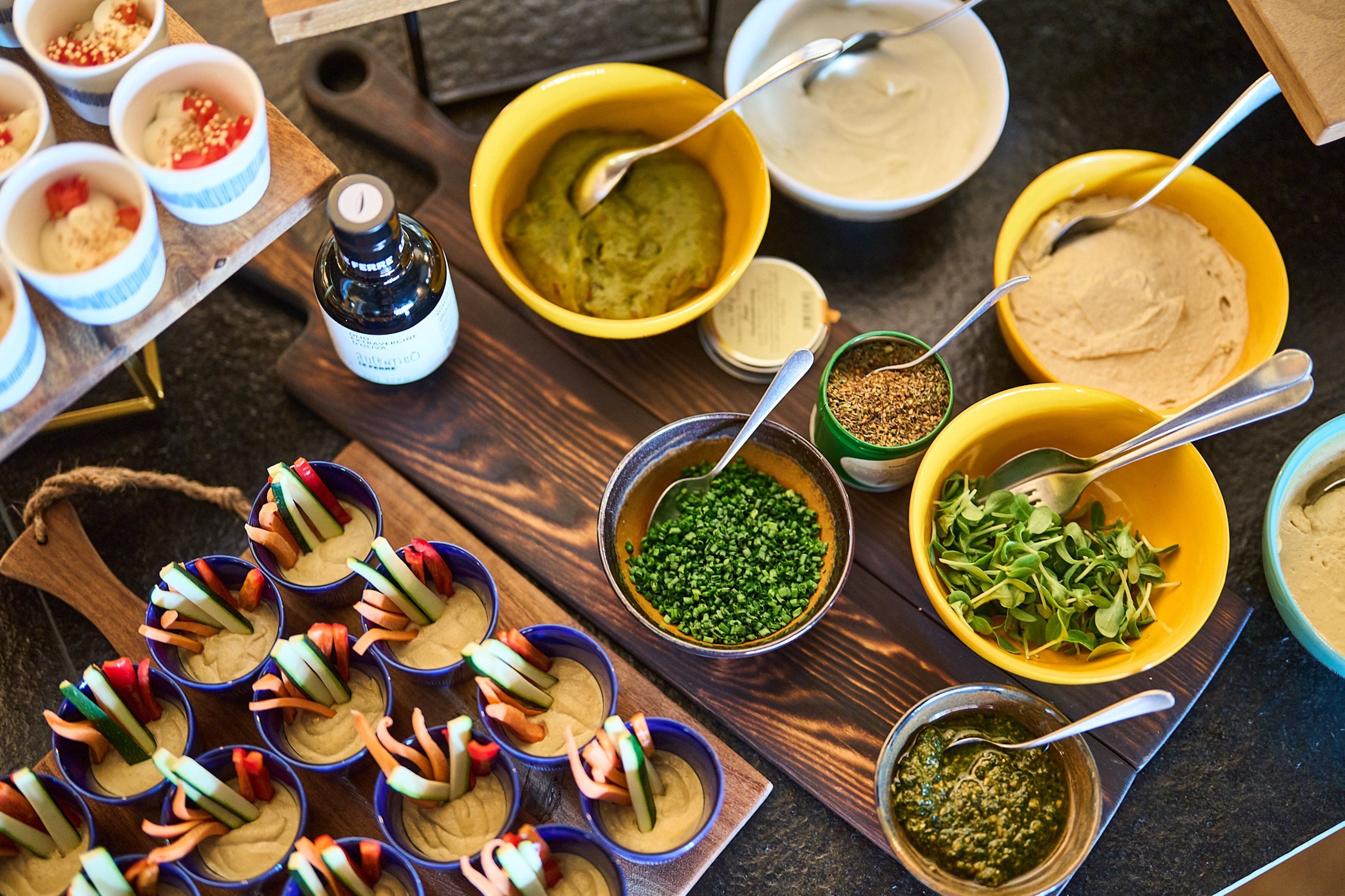On une table en bois, on peut voir une variété d’aliments et d’ustensiles, notamment des bols de houmous, une bouteille de sauce et des bols de légumes.