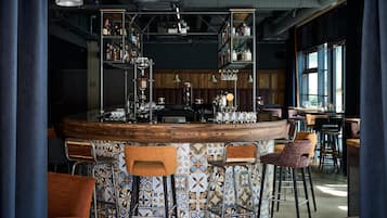 Zona de bar con mostrador redondo, taburetes y estantes con botellas.