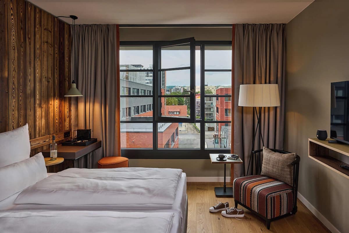 A hotel room with a large window, a bed, a desk, a chair, and a television.