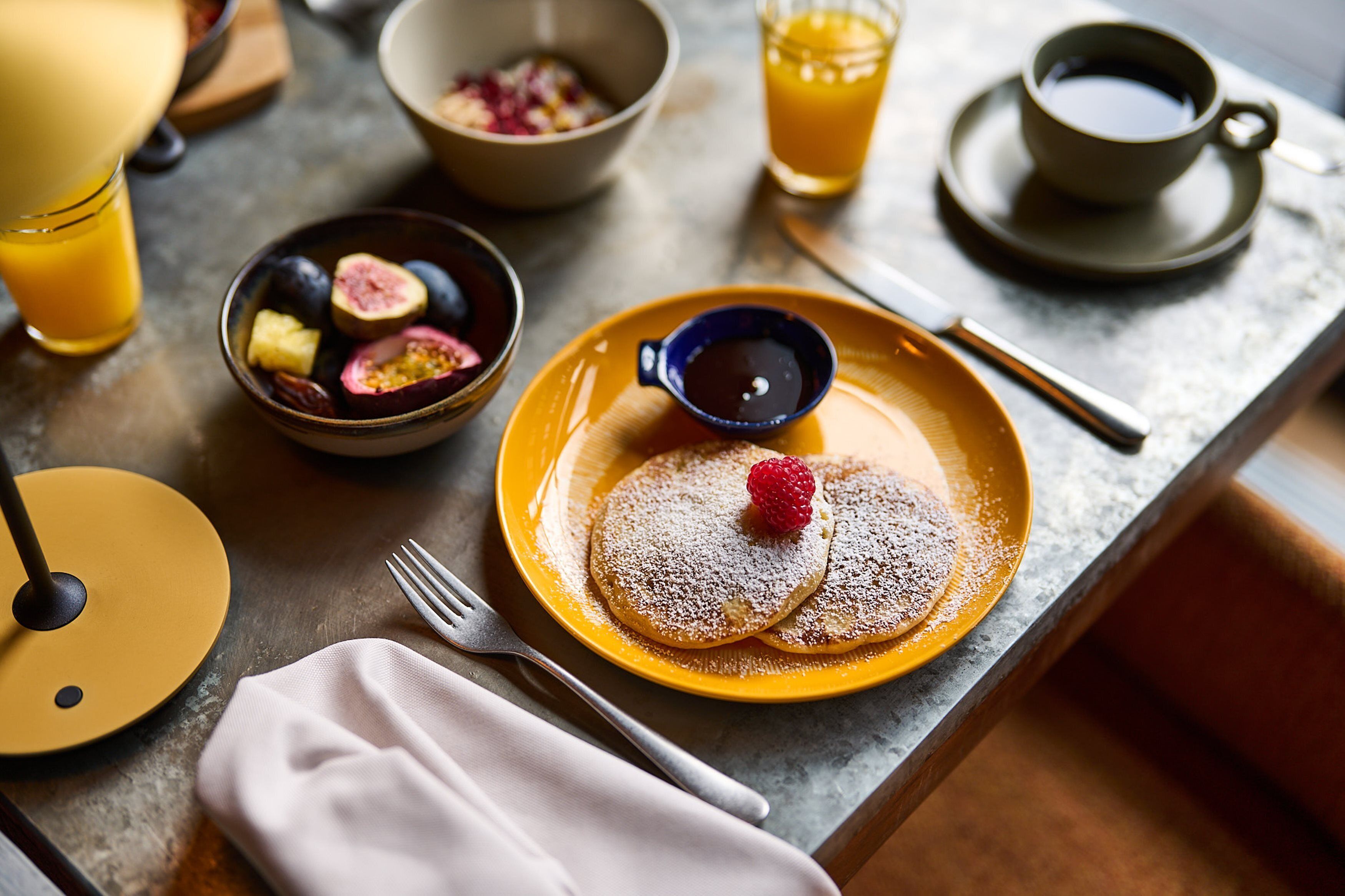 A breakfast setting with pancakes, a cup of coffee, and a bowl of fruit.