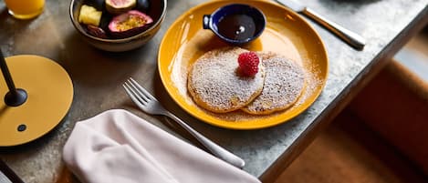 Desayuno con tortitas, una taza de café y un bol de fruta.