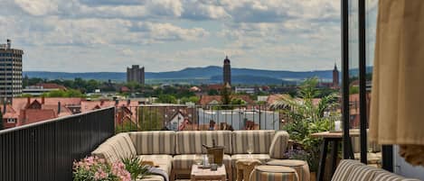 Una terraza en la azotea con un conjunto de sofás, una mesa con un jarrón y vistas de la ciudad, incluyendo una torre.