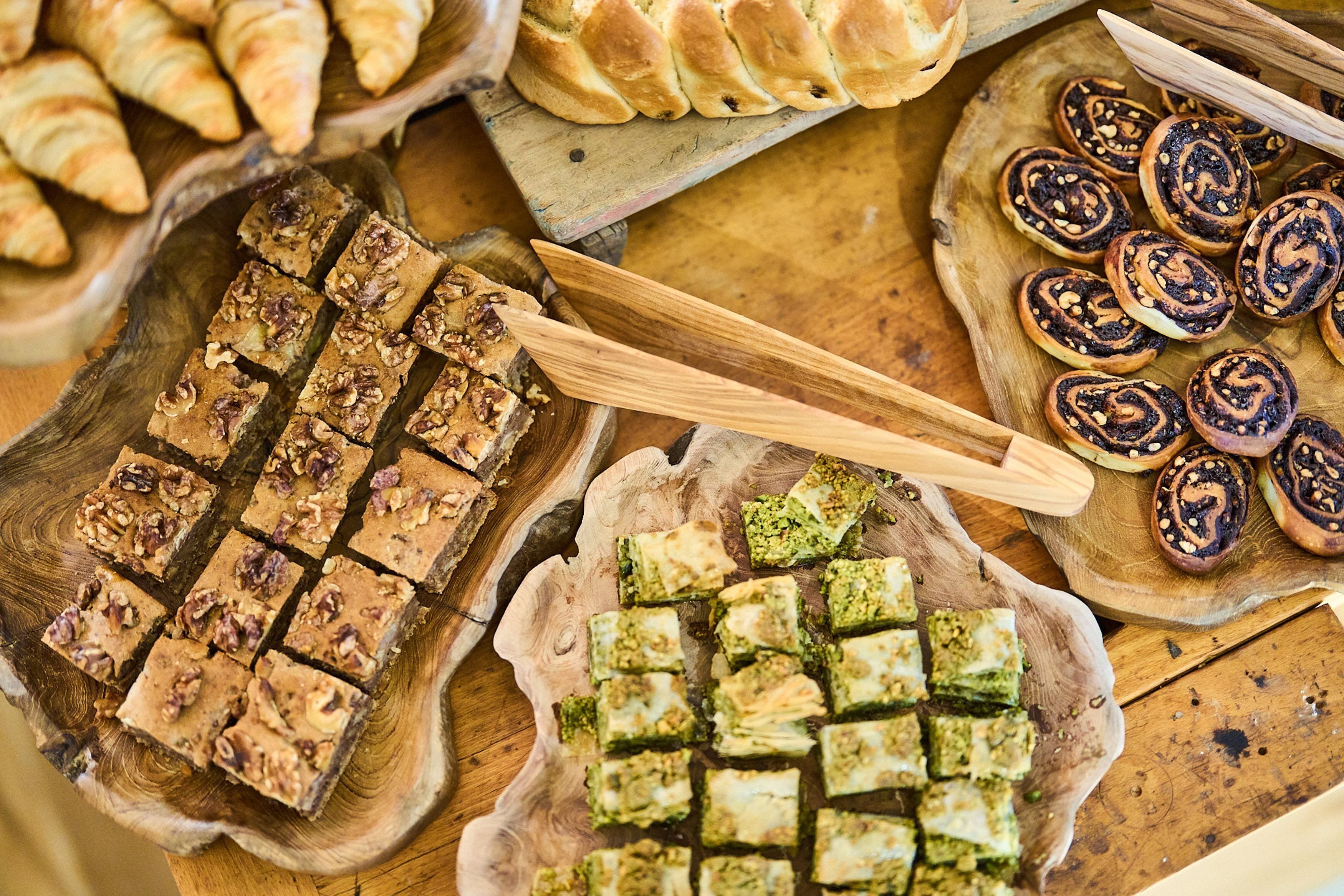 A wooden table with various baked goods including pastries and nut-topped bars.