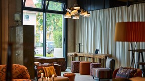 A cozy living room with a large window, a wooden table, and patterned furniture. - FREIgeist Göttingen Nordstadt - A Member of Design Hotels™ (Goettingen)