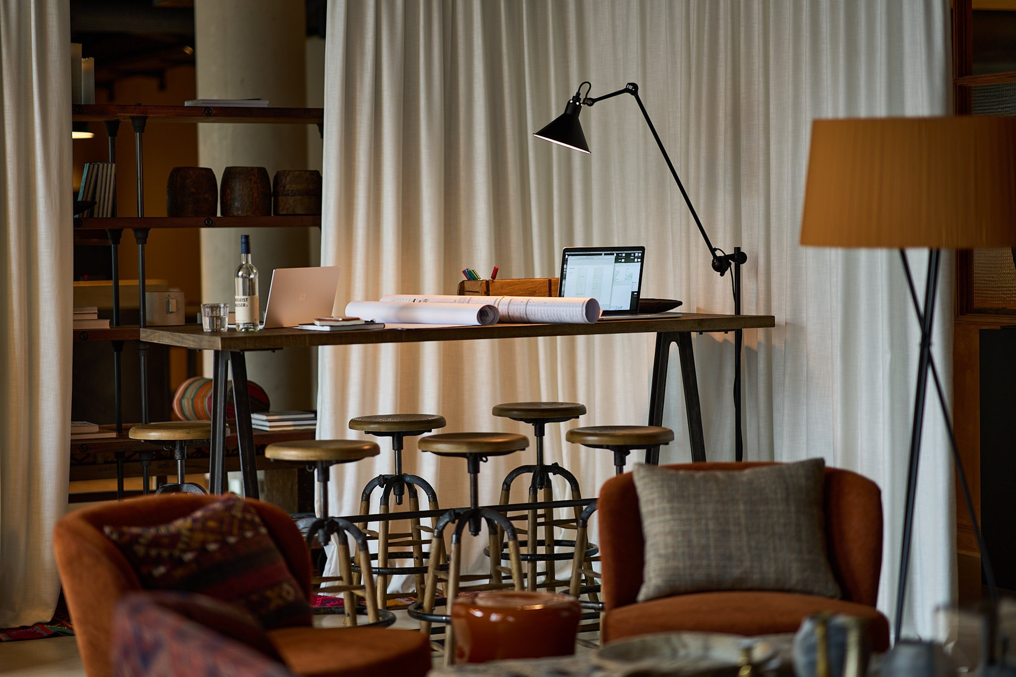 A modern living room with a high table, bar stools, a sofa, and a lamp.