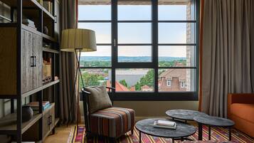 A room with a large window, a bookshelf, a striped armchair, a small table, and a colorful rug.