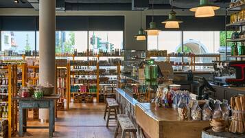 Una tienda bien iluminada con estanterías de madera llenas de diversos productos, un mostrador con artículos envasados y un amplio ventanal con vistas a la ciudad.