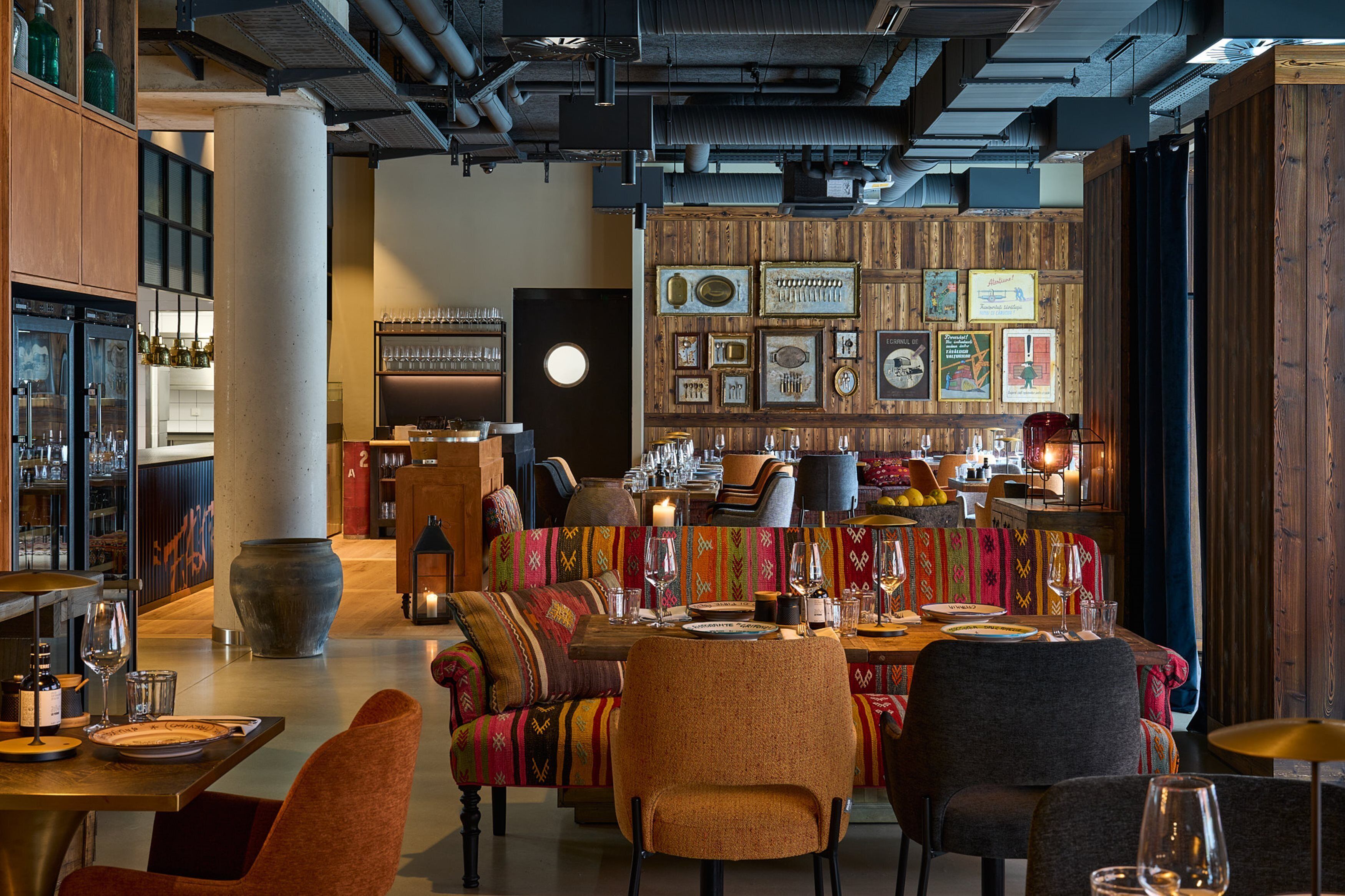 A restaurant interior with a bar area, seating with colorful upholstery, and a wall decorated with framed pictures and a large clock.