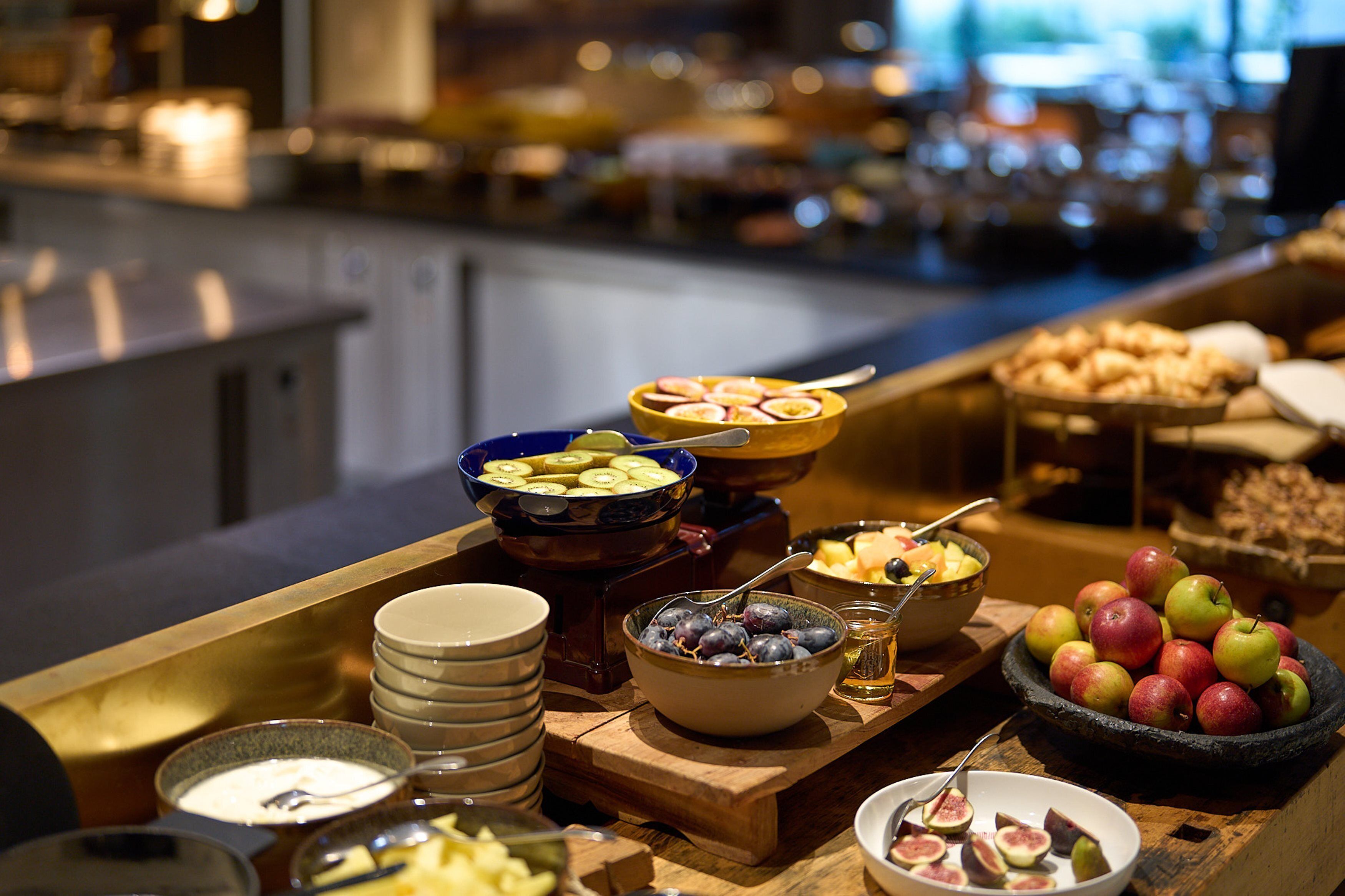 A buffet with various fruits, bowls of yogurt, and a selection of cheeses.