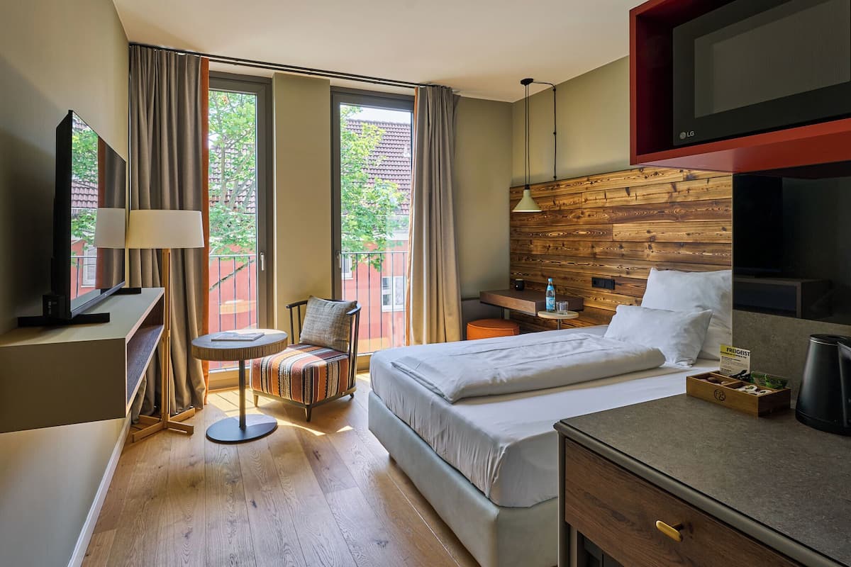 A hotel room with a bed, desk, chair, TV, and a view of the outdoors.