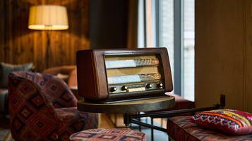 A vintage radio on a small table in a cozy room with patterned furniture and a lamp in the background.