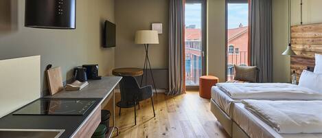 Une chambre d’hôtel comprenant un lit, un bureau avec une chaise, une lampe sur pied, un téléviseur et une vue sur les bâtiments environnants.