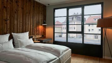 Een slaapkamer met een groot raam, een houten paneelwand en een nachtkastje met een lamp.