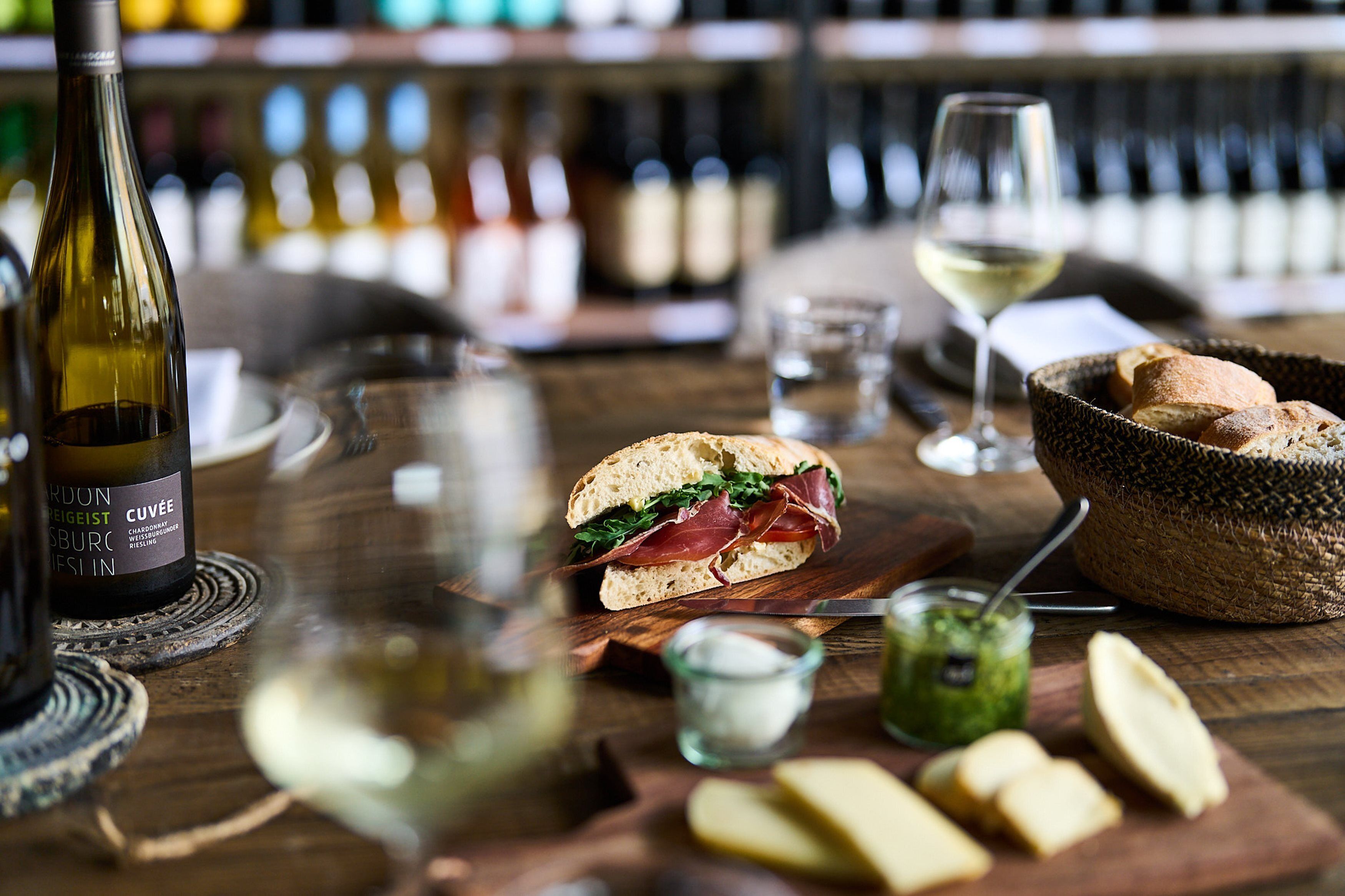 A wooden table with a bottle of wine, a sandwich, a glass of wine, and some bread.