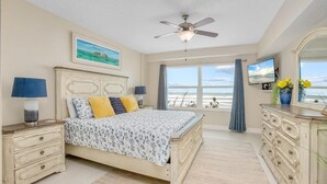Ein Schlafzimmer mit Bett, Deckenventilator, Fernseher und Blick auf den Ozean.