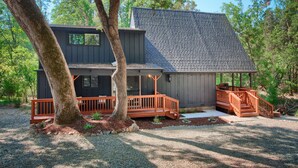 A modern two-story house with a grey roof and wooden deck, surrounded by trees. - Modern A-Frame next to a creek, minutes to Bass Lake and close to Yosemite  (Oakhurst)