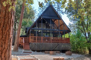 A cabin with a wooden deck, large windows, and a sloped roof, surrounded by trees. - Modern A-Frame next to a creek, minutes to Bass Lake and close to Yosemite (Oakhurst)