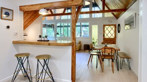 A modern kitchen with wooden accents, a bar area with stools, and a dining space with wooden chairs and a bench. - Modern A-Frame next to a creek, minutes to Bass Lake and close to Yosemite  (Oakhurst)