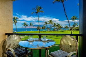 A balcony with a glass table and wicker chairs, overlooking a golf course and ocean. - Enjoy Your Oceanside Dream at Kihei Surfside (Kihei)