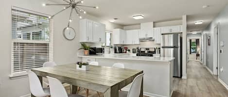 Una cocina moderna con armarios blancos, una mesa de comedor de madera y una isla central.