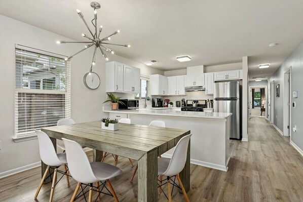 A modern kitchen with white cabinets, a wooden dining table, and a central island.