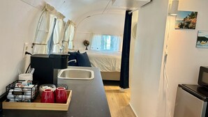 Habitación compacta con cama, kitchenette pequeña, lavamanos y ventana con cortinas.